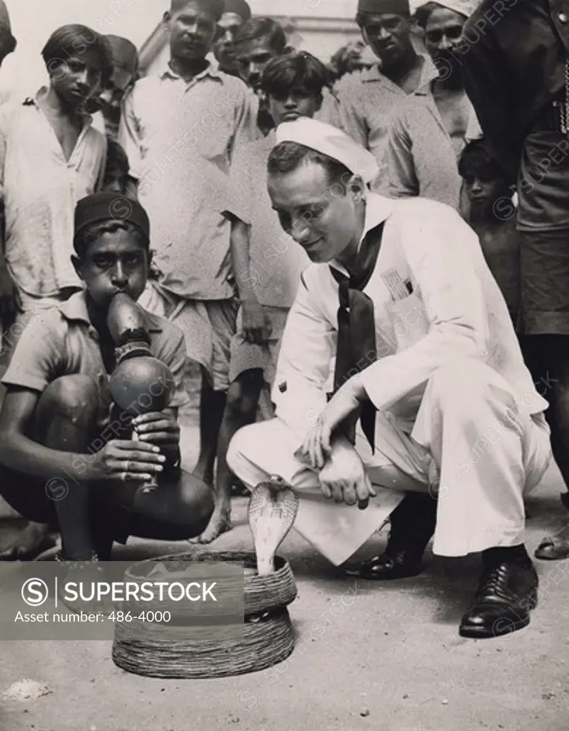 India, Bombay, Henry V. Keck watching snake charmer on street, Coast Guardsman Henry V. Keck, seaman, 1/c of 152 Hopkinson Ave, Brooklyn, takes in snake charmers performance on street in Bombay while on shore liberty from a transport. Keck is a veteran of both Atlantic and pacific war theaters