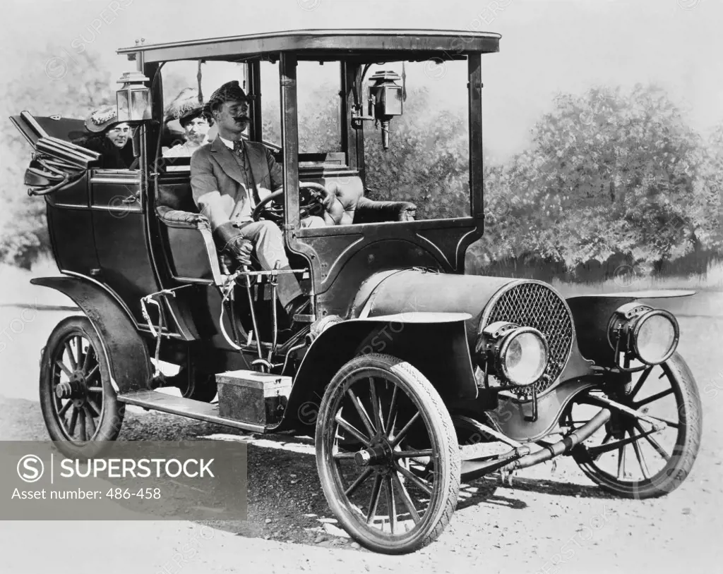 Mature man driving a car with two mid adult women sitting behind him, 1908 Franklin