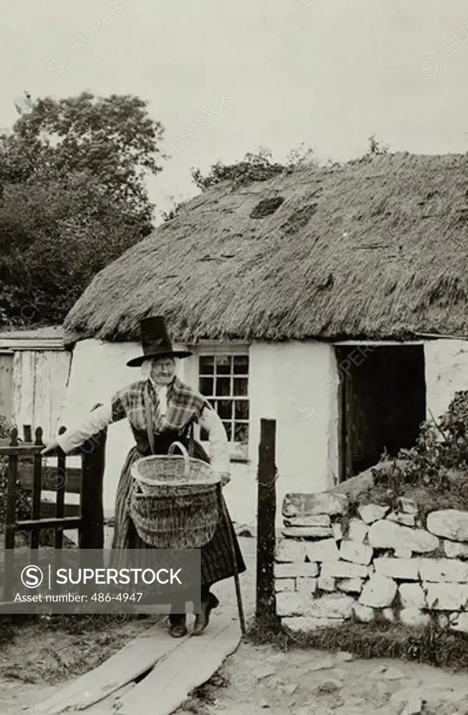 UK, Wales, Portrait of senior woman in traditional clothing standing in front of old hut