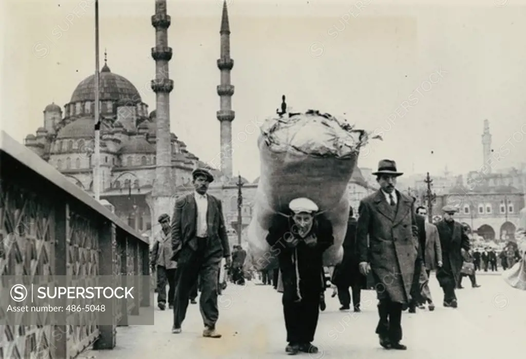 Turkey, Istanbul, Porter called ""hamal"" carrying heavy load, Turkey, Istanbul, Porter called ""hamal"", shoulders his heavy load as he plods along. The porters are Anatolian peasants who come to the city for a few years, live frugally, salt away their modest earnings, then retire to their home villages with small fortune by village standards. They may make from 10 to 20 lira (2, 8 lira to $1) a day. Often a number share as sleeping quarters