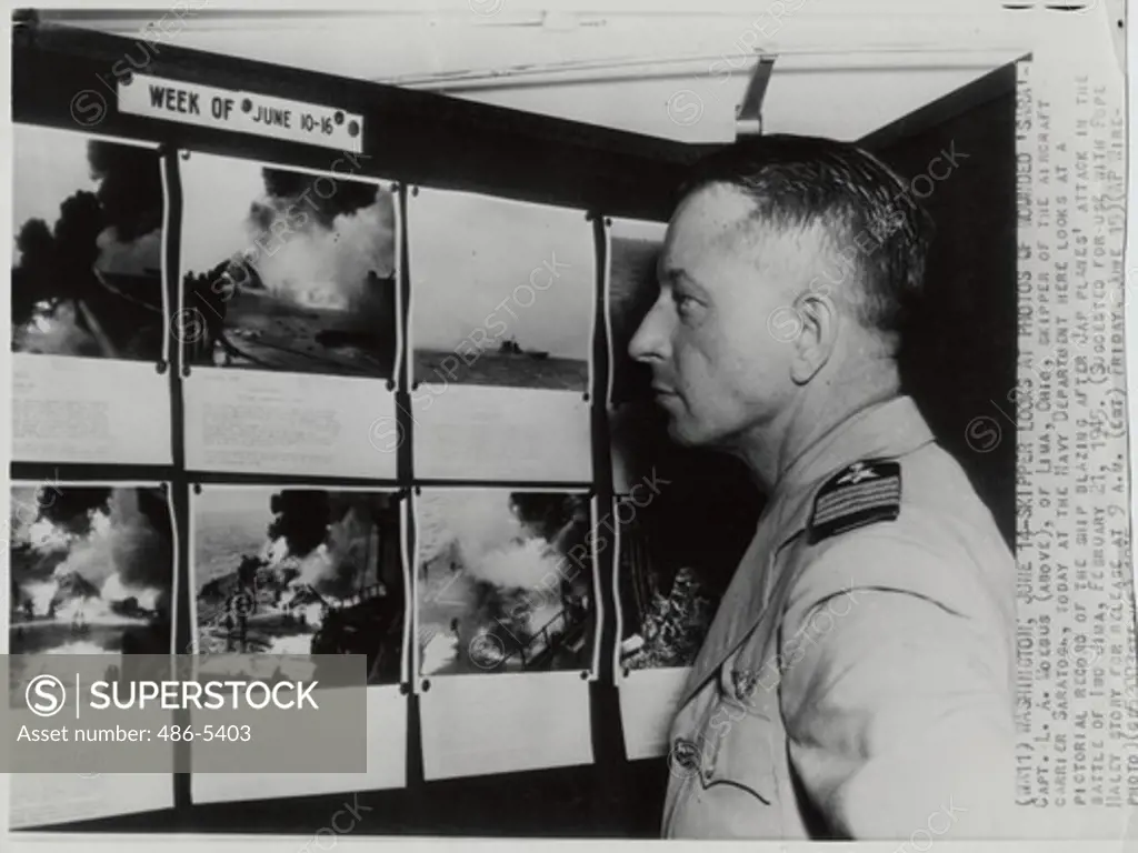Capt. L. A. Moebus, Skipper of aircraft carrier Saratoga looking at pictorial record of ship blazing after Japanese planes' attack in battle of Iwo Jima, 1945