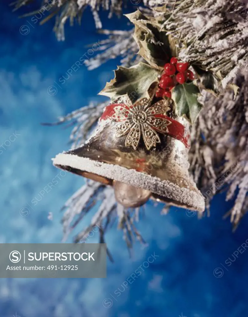 Close-up of a bell with holly leaves and berries hanging on a Christmas tree