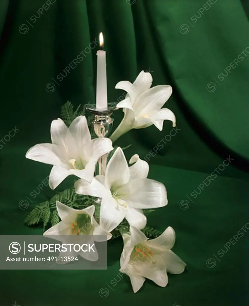 Burning candle near Easter Lily flowers