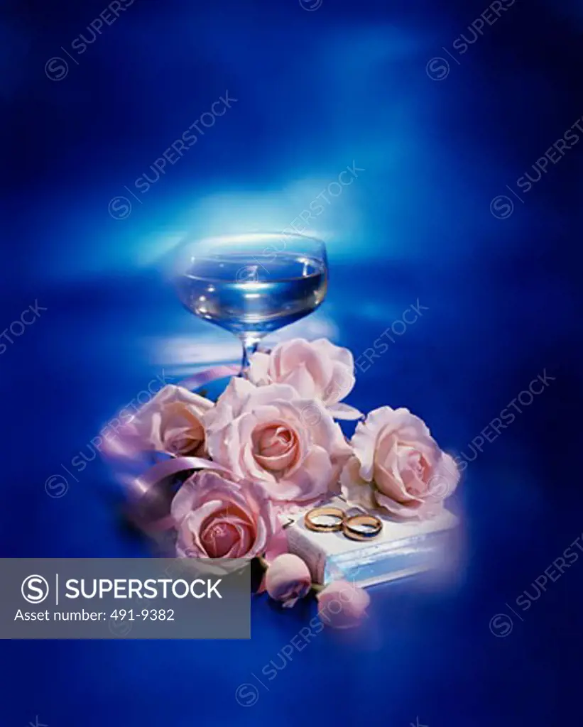 Roses with two wedding rings and the Bible near a wineglass