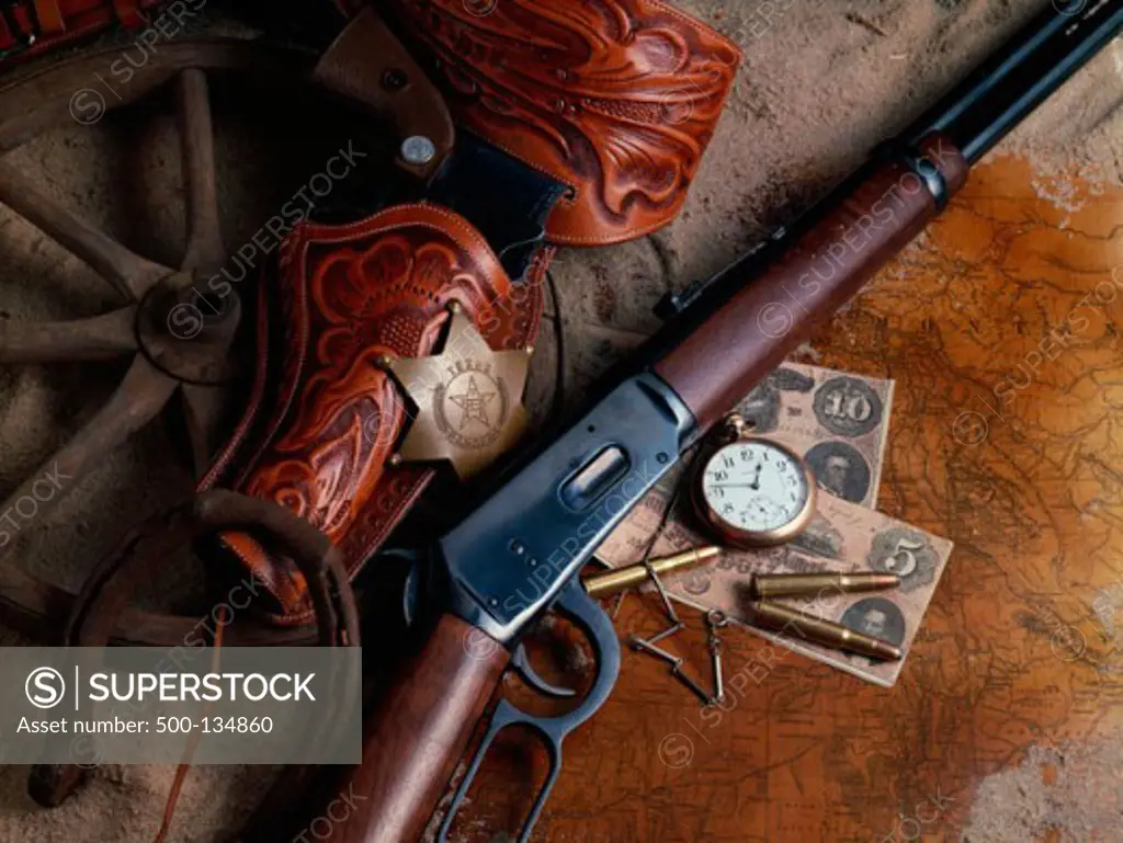 High angle view of a rifle and a revolver beside money and a watch
