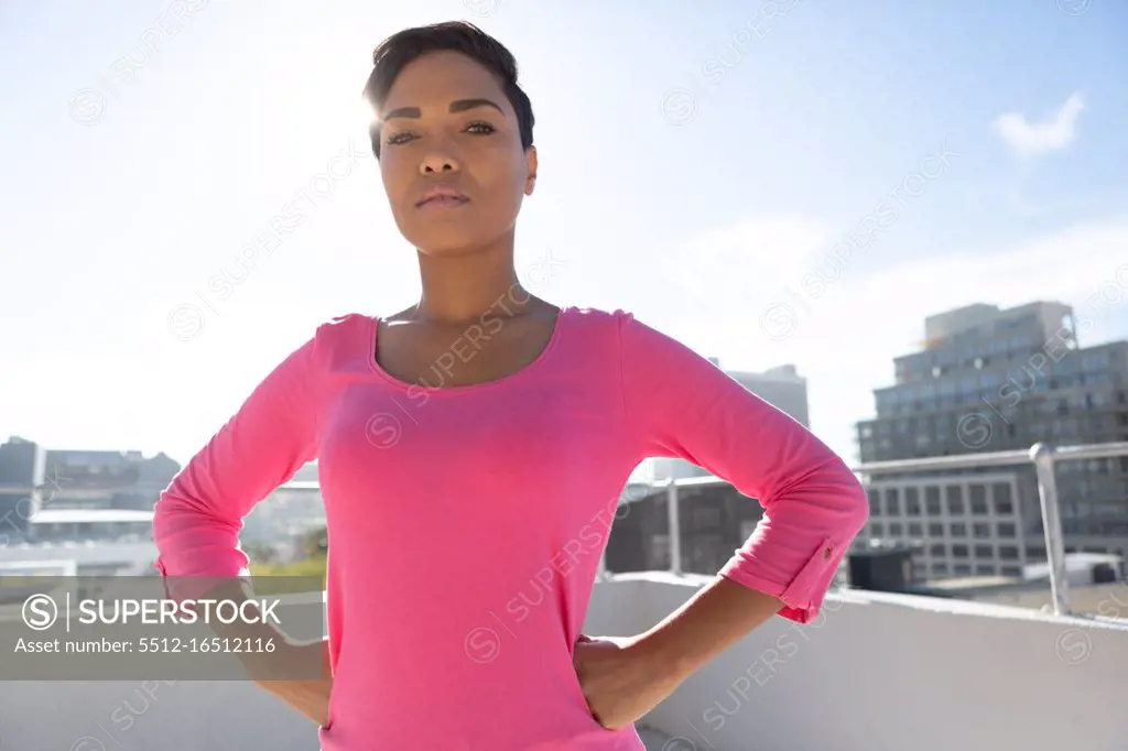 Serious looking woman standing confident for breast cancer awareness in pink shirt against urban background