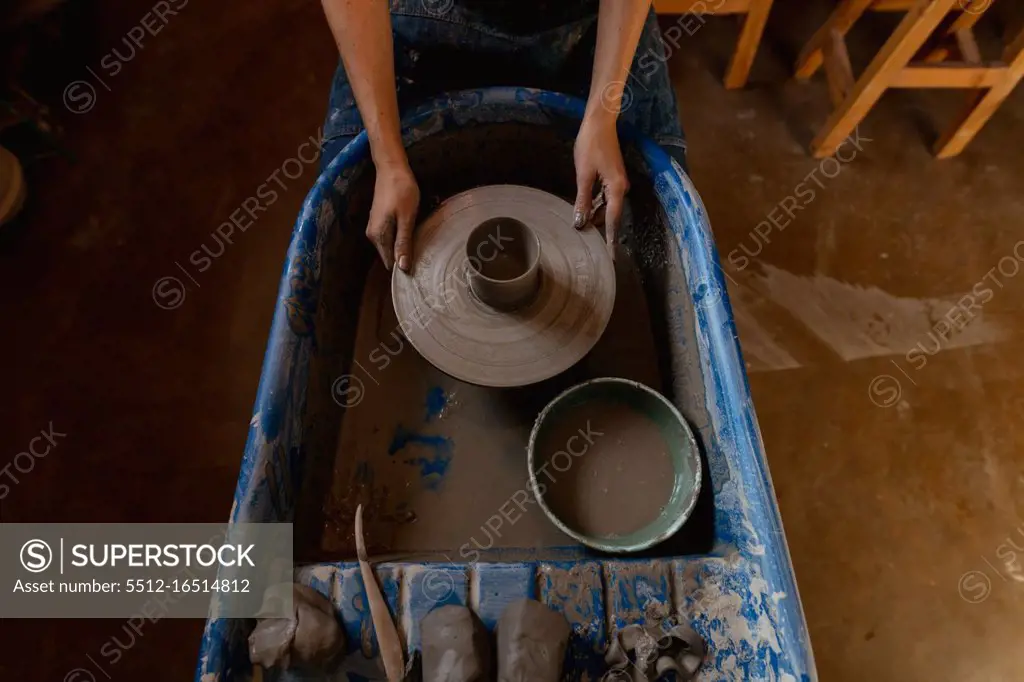 Elevated view of the hands of a young Caucasian female potter holding a potters wheel with a pot on it in a pottery studio