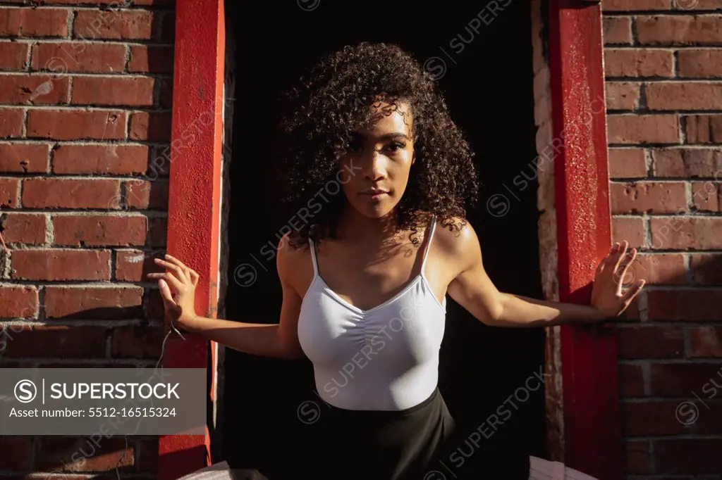 Front view close up of a young mixed race female ballet dancer standing in a doorway in a brick wall and looking straight to camera