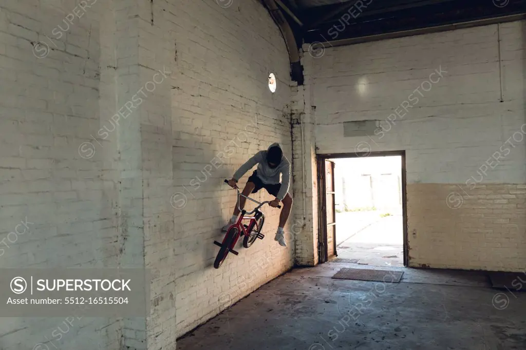 Front view of a young Caucasian man wallriding a BMX bike in an empty corridor at an abandoned warehouse