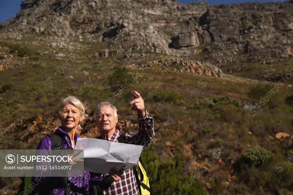 Front view close up of a mature Caucasian man and woman reading a map and pointing during a walk in a rural setting, with mountains in the background