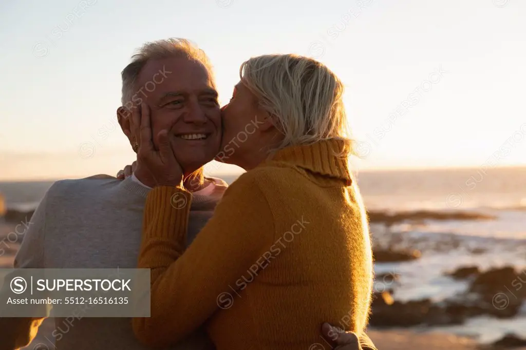 Side view close up of a mature Caucasian man and woman embracing and kissing by the sea at sunset