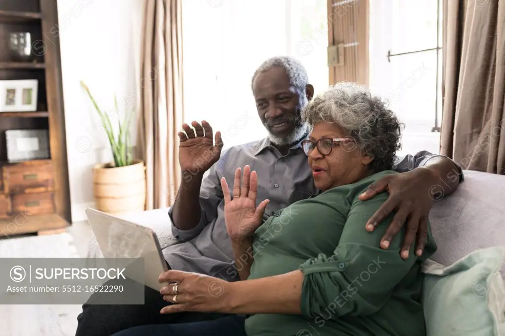 A senior African American couple spending time at home together, social distancing and self isolation in quarantine lockdown during coronavirus covid 19 epidemic, using a tablet, making a video call to friends or relatives, waving