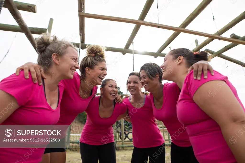 Multi-ethnic group of women all wearing pink t shirts at a boot camp training session, exercising, smiling motivating and hugging each other. Outdoor group exercise, fun healthy challenge.