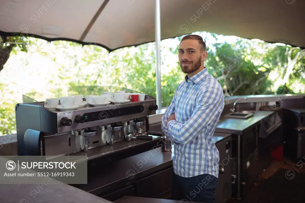 Portrait of male owner standing with arms crossed at outdoor café