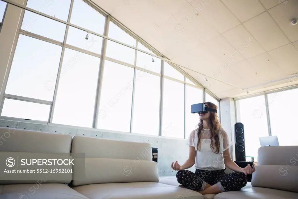 Full length of businesswoman mediating while using virtual reality on sofa in office