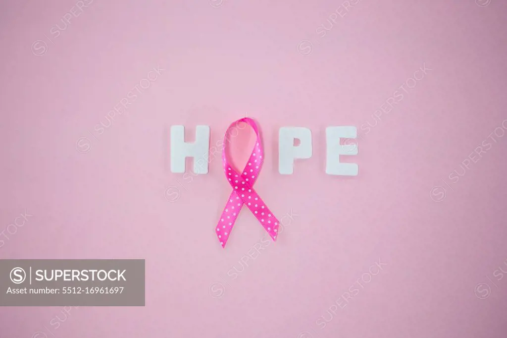 Overhead view of spotted Breast Cancer Awareness ribbon with HOPE text on pink background