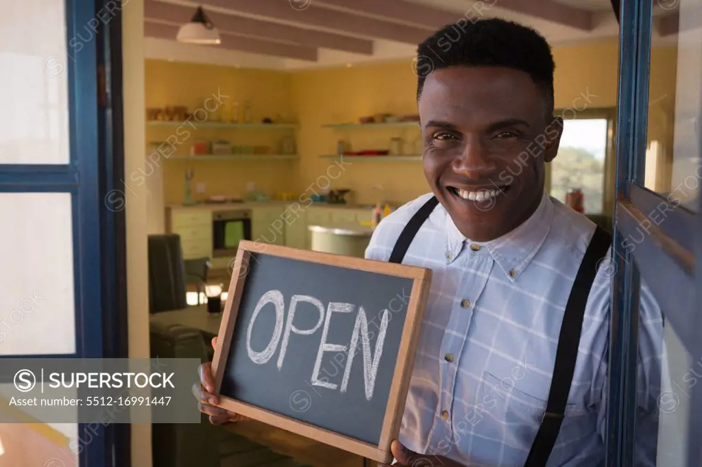 Male owner holding chalkboard with open sign at restaurant