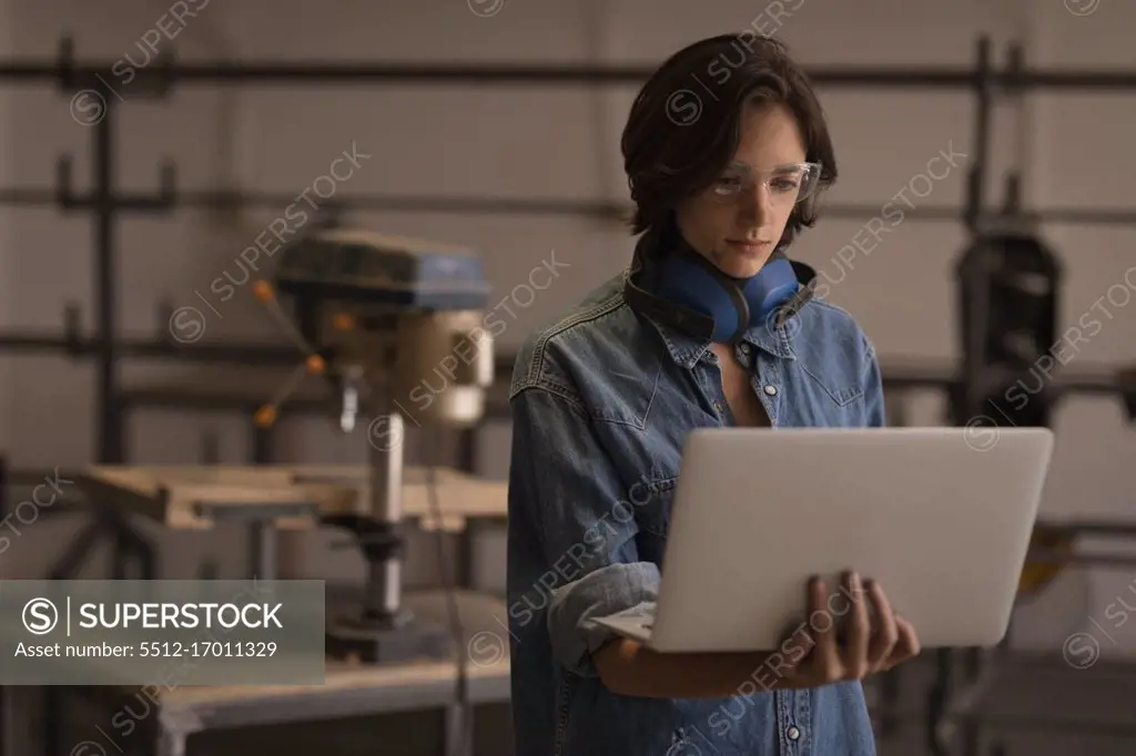 Young female welder using laptop in workshop