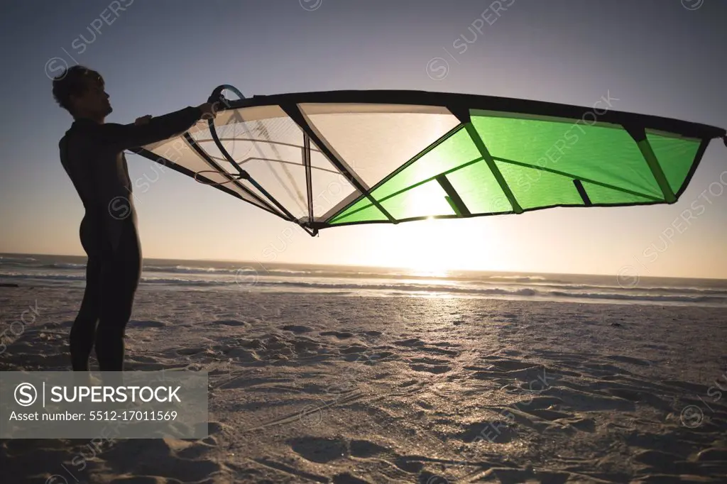 Male surfer holding a kite on the beach at dusk