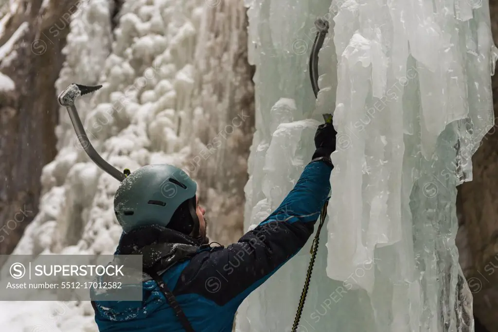Male rock climber climbing ice mountain during winter