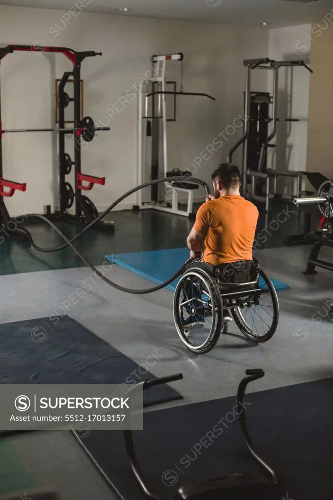 Handicapped man on wheelchair exercising with battle ropes in gym