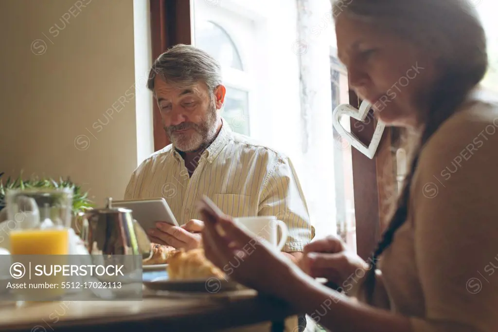 Senior couple using digital tablet and mobile phone while having breakfast at home