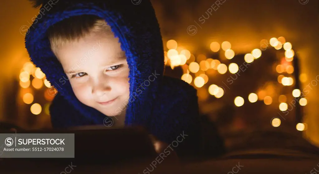 Close-up of boy in blue jacket using digital tablet against Christmas lights