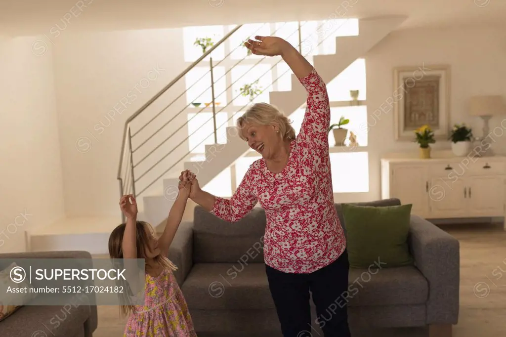 Grandmother and granddaughter dancing in living room at home
