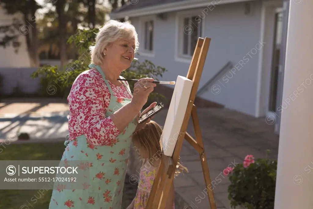 Side view of senior woman painting on canvas in the garden