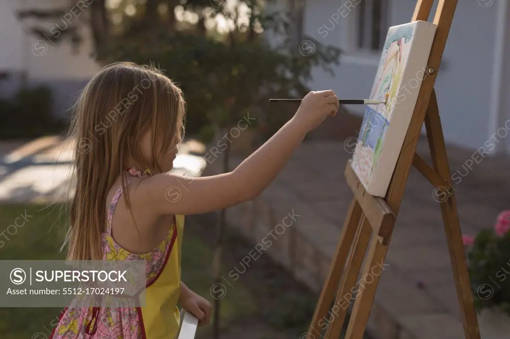 Side view of girl painting on canvas in the garden