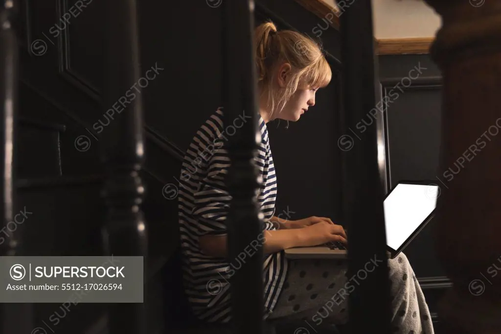 Side view of woman using laptop on stairs at home