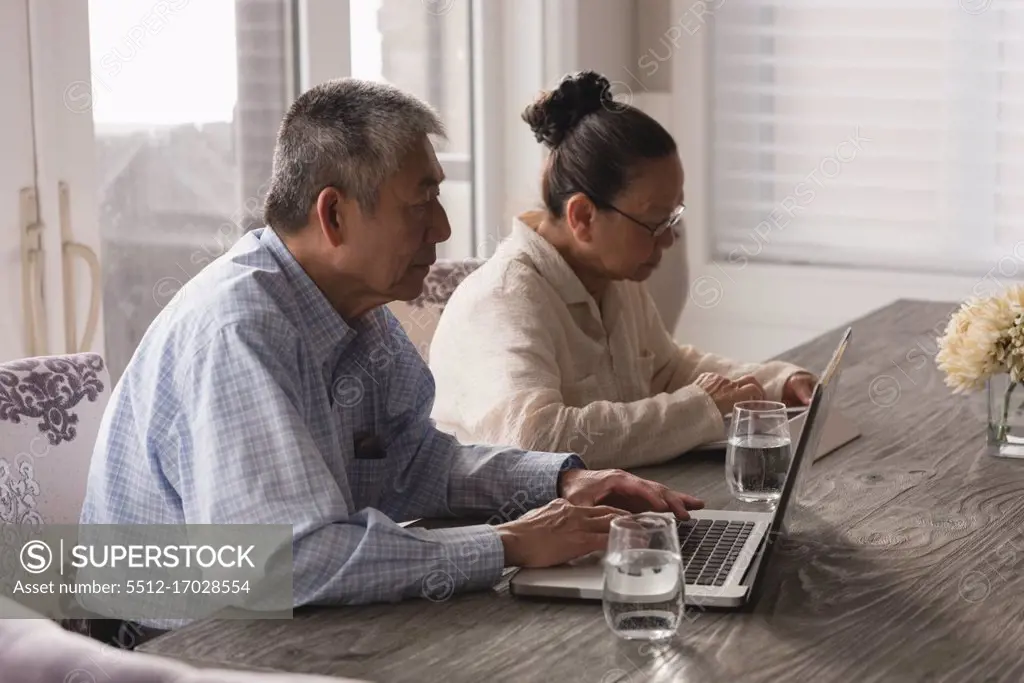 Senior couple using laptop and digital tablet on dining table at home