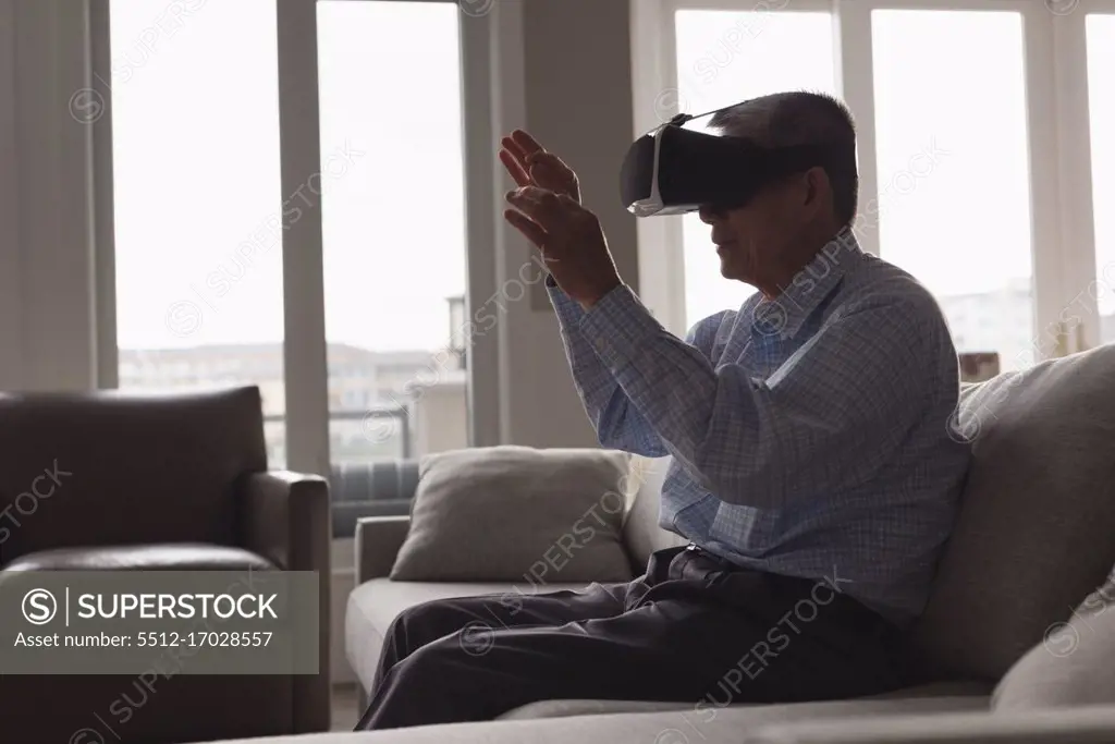 Senior man using virtual reality headset on sofa in living room at home
