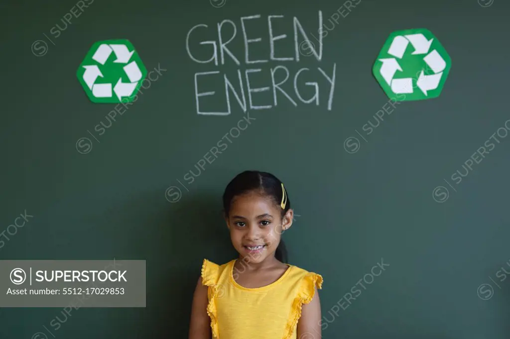 Front view of smiling schoolgirl standing against green energy board in classroom of elementary school