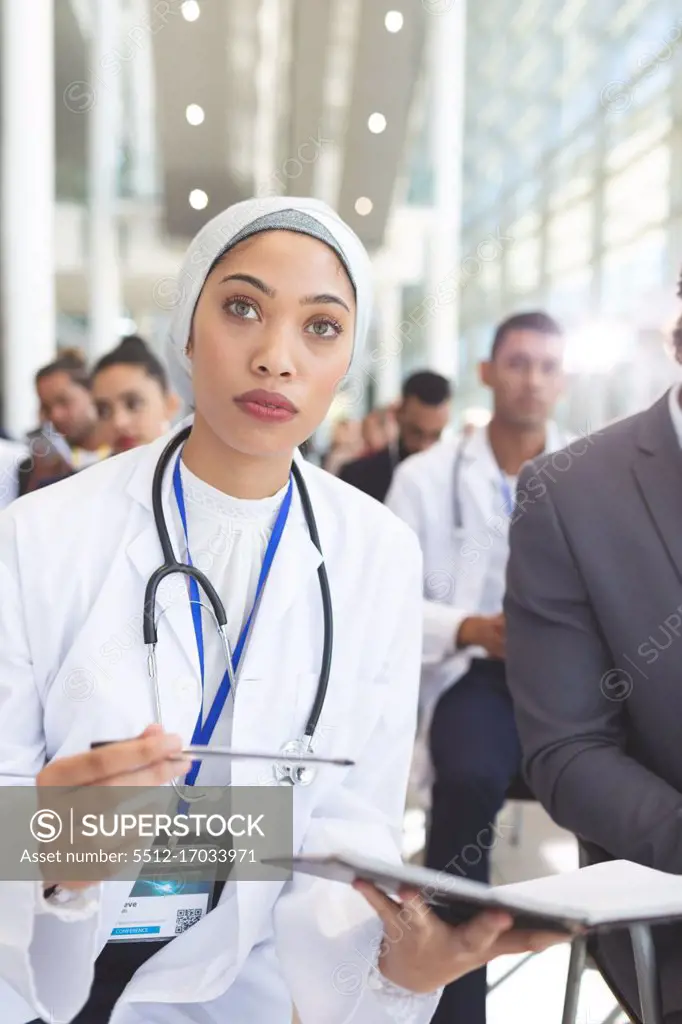 Front view of mixed race  female doctor with notebook and pen attending seminar in conference room
