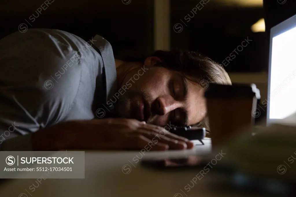 Side view of young Caucasian male executive sleeping at desk in a modern office