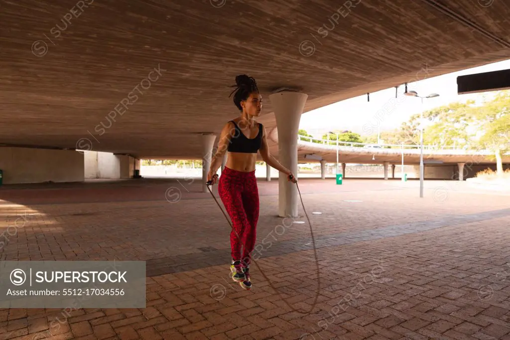 Side view of a young fit mixed-race girl training with a jumping rope under a yard on the afternoon