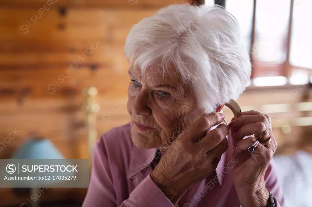 Front view of an active senior woman wearing a hearing aid in her ear in bedroom at home the