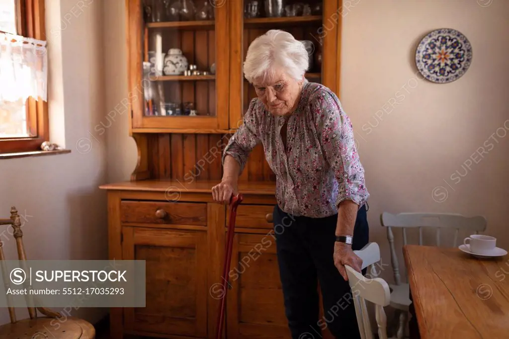 Front view of an active senior woman walking with a cane in the kitchen at home