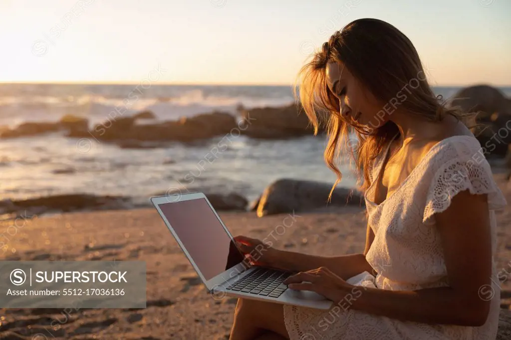 Side view of beautiful woman using laptop at beach