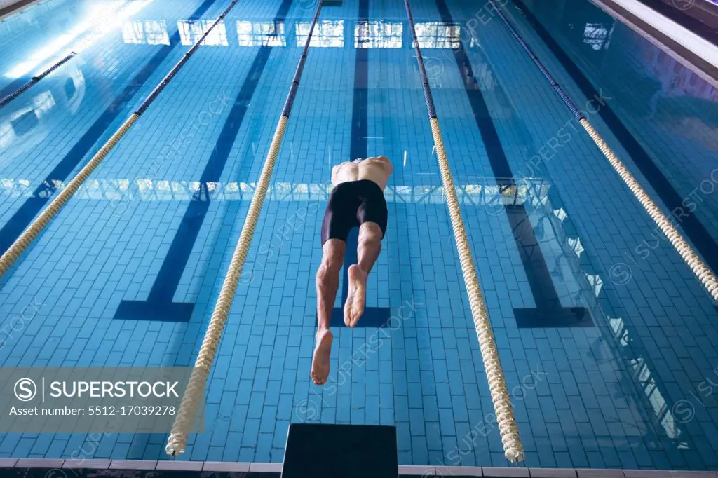 Rear view of a male Caucasian swimmer wearing a white swimming cap diving in the pool