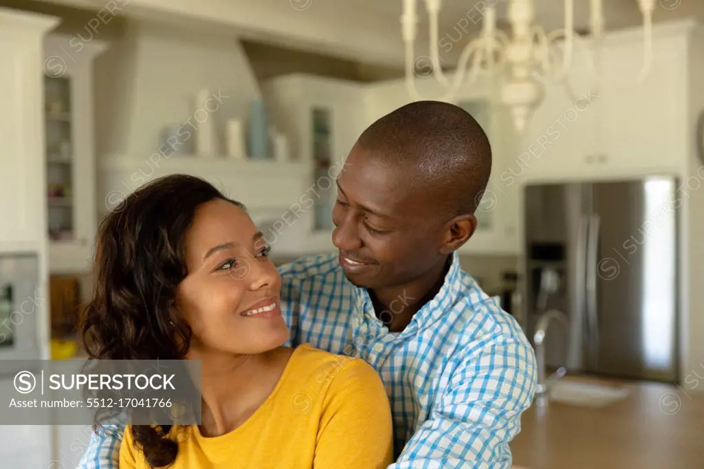 Self isolation in quarantine lock down. front view close up of an african american man and a mixed race woman at home in their luxury kitchen, embracing and smiling at each other