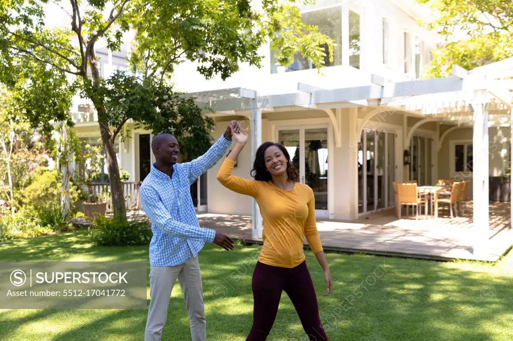 Self isolation in quarantine lock down. front view of an african american man and a mixed race woman outside their house in the garden on a sunny day, having fun holding hands and dancing together