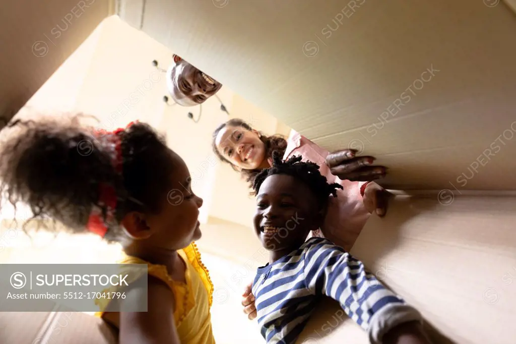 Low angle view of a mixed race couple and their young son and daughter looking at each other and reaching into a packing box they are opening in the hallway of their new home, and smiling