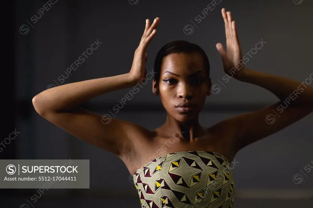Portrait of a mixed race female dancer wearing yellow dress, dancing in a studio with her hands up.