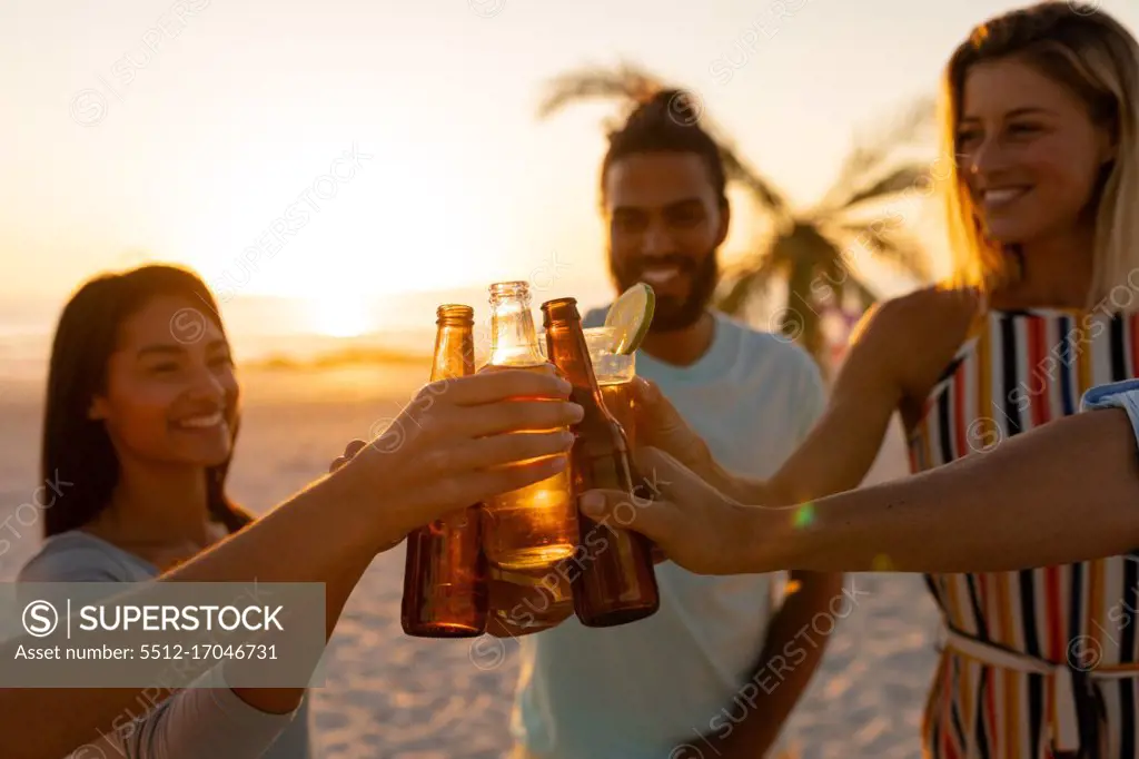 A multi-ethnic group of friends enjoying their time together on a beach during sunset, drinking beer and drinks, making a barbecue, making a toast