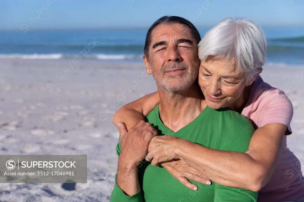 Senior Caucasian couple enjoying time at the beach, a woman is embracing a man from behind