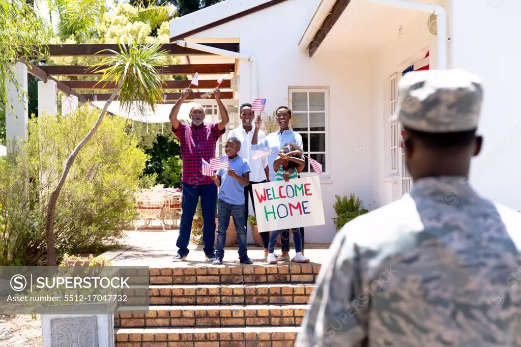 African American three generation family standing by their house with a banner, welcoming an African American solider wearing uniform.