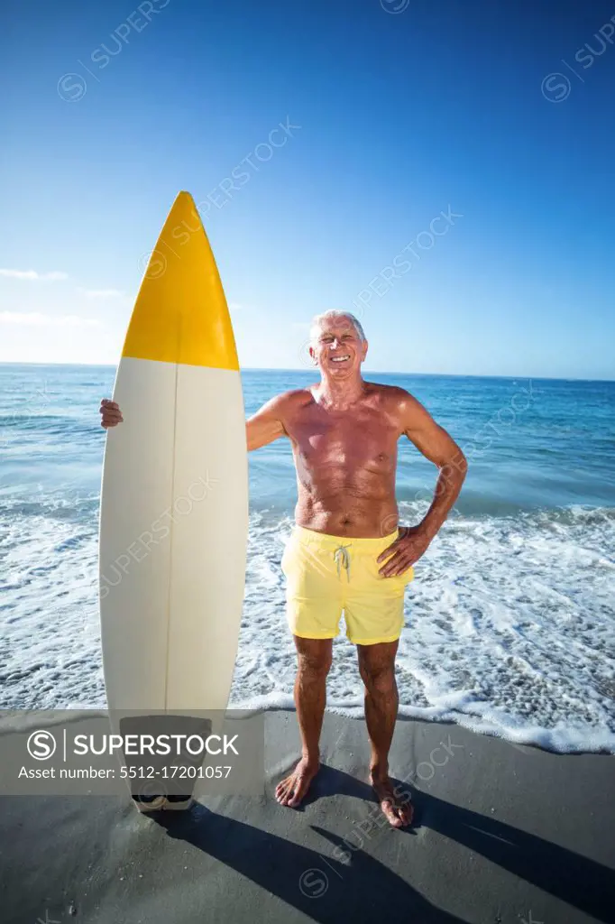 Senior man posing with a surfboard at the beach