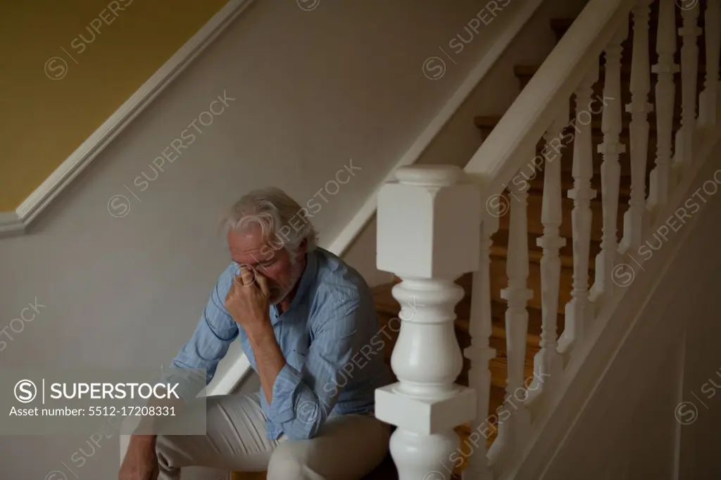 Worried senior man sitting on stairs at home